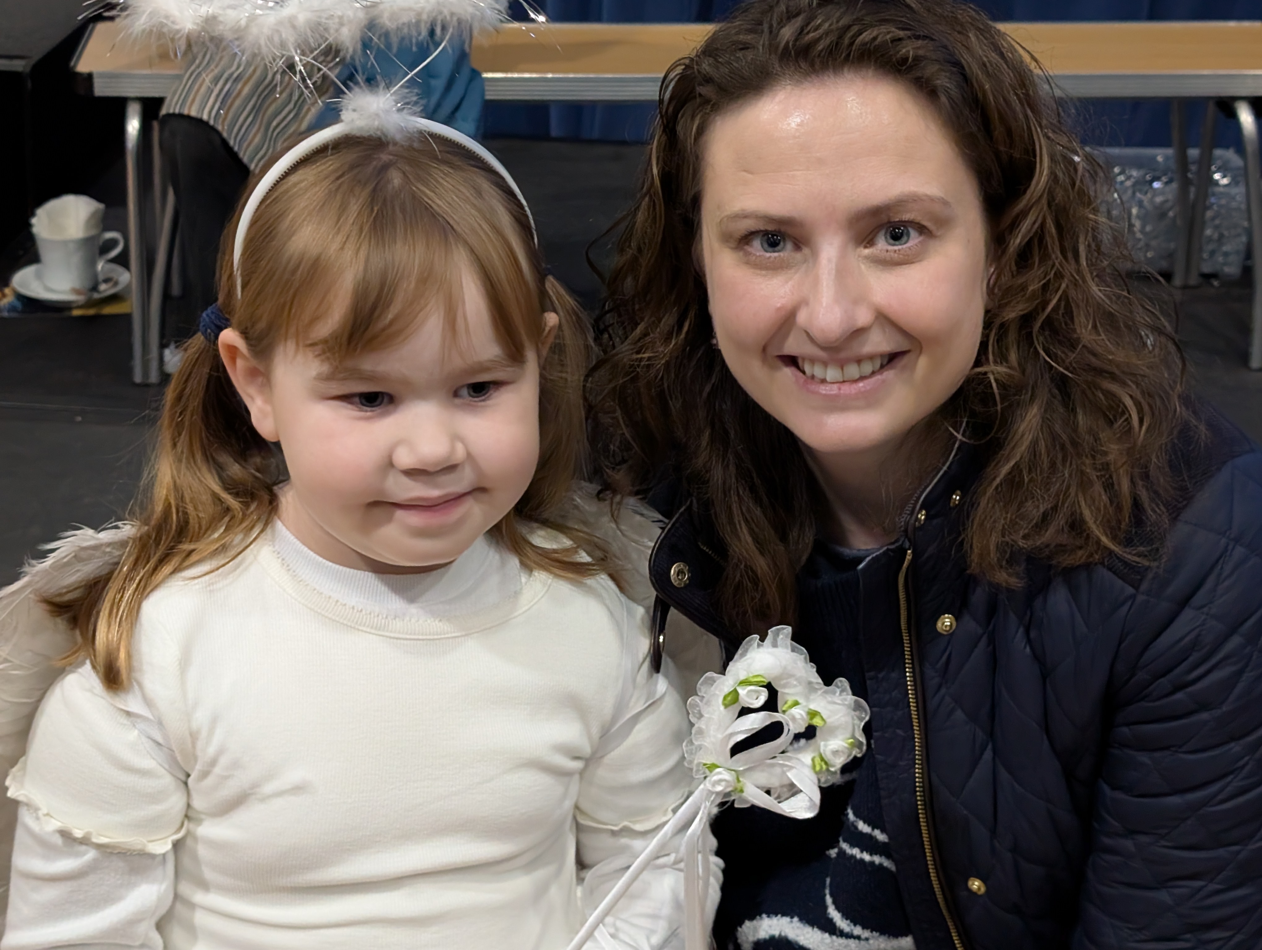 Esther and her daughter Phoebe at a school Christmas event. Phoebe is dressed as an angel, holding a wand — she has that careful, watchful expression that parents of SM children will recognise instantly.